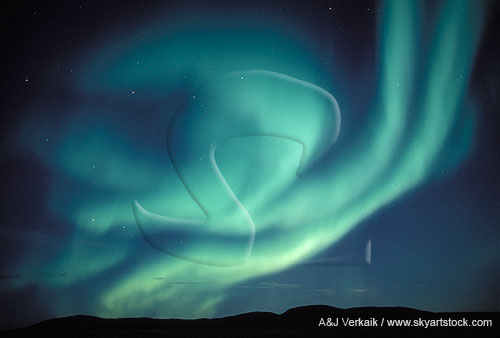A blue-green phantom (Aurora Borealis) looms over arctic hills.