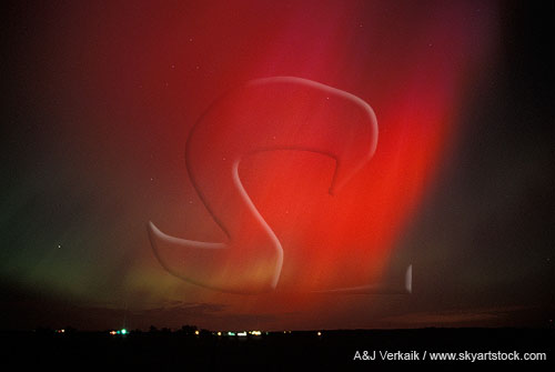 Sweeping red curtains of northern lights over farm lights