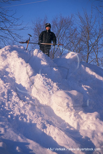 A young boy stands atop a very large snowbank