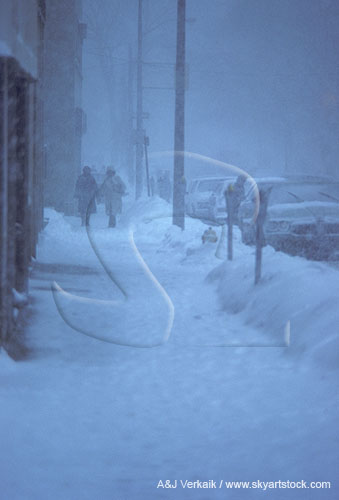 People walk down a city sidewalk in a snowstorm