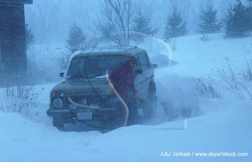 Digging out a car in a snow storm with wind and blowing snow