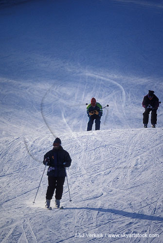 Skiers add tracks to the snow on a ski slope 