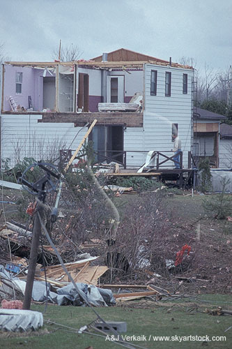 A house ripped open, with twisted satellite dish and tornado debris