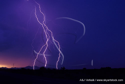 Cloud-to-ground lightning bolts in a twilight sky.