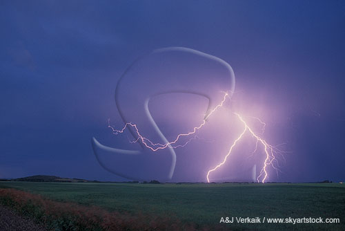 Forked cloud-to-ground lightning strikes a field in daylight