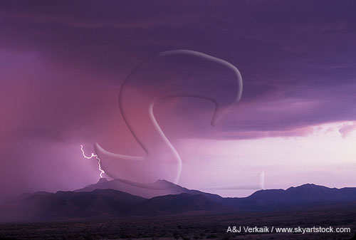 A lone lightning bolt strikes a mountaintop in pink sunset light 