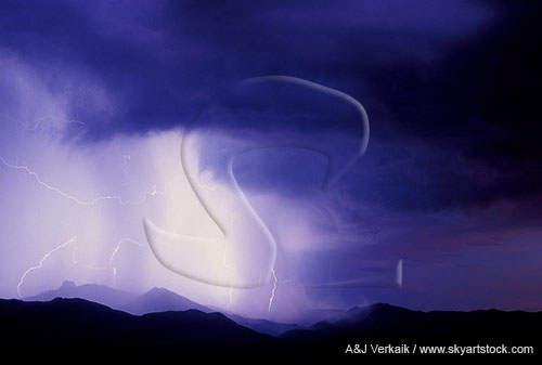 Lightning lends a mysterious glow to a mountain rain shower at twilight