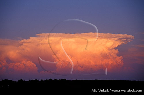 A distant supercell storm cloud has exploded to the east at sunset
