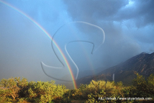 A close double rainbow shines on a mountain rain shower