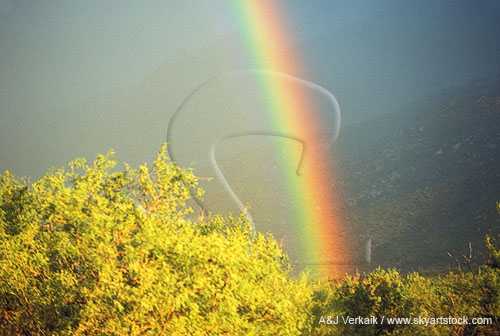 A brilliant rainbow glows at the foot of a mountain