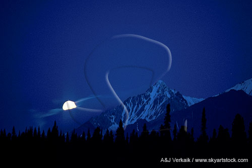 A meditative full moon rises at dusk in the mountains