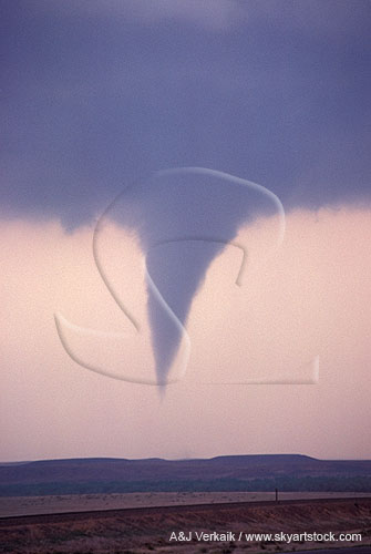 A tornado backlit at twilight in open country