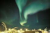Green curtains of Aurora Borealis over a lit-up arctic settlement