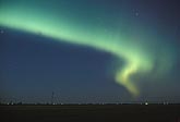 A band of Aurora Borealis arcs over a prairie landscape
