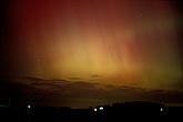 Red and yellow northern lights streak down over a farm