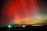 Glorious, brilliant red and green beams of northern lights over a farm