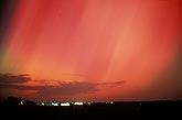 The world ablaze with red curtains of Aurora Borealis over farm lights