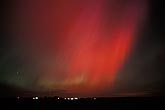 Sweeping red curtains of northern lights over farm lights