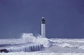 Waves crash around a beacon (lighthouse) in high winds