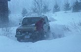 Digging out a car in a snow storm with wind and blowing snow