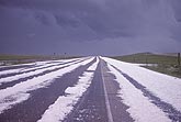 Heavy hailfall covers a highway under a leaden stormy sky