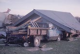 Tornado damage to vehicles, an ATV and a truck under a drive shed