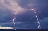 Two close and finely detailed lightning bolts glow pink in the daylight sky