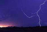 A single close lightning bolt against a red and blue sunset