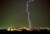 A single bolt of lightning strikes down into a city skyline at night