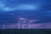 Lightning bolts over a field in a pale purple twilight