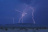 Several cloud-to-ground lightning bolts in desert hills at twilight
