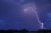 A single lightning bolt reaches out from a storm at twilight