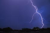 A single brilliant lightning bolt cuts through a deep blue dusk sky
