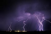 Jagged cloud-to-ground lightning bolts over city lights