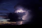 A mountain storm cloud lights up with a single lightning strike at dusk