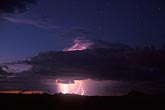 Lightning makes a storm cloud glow in a surreal colorful sunset