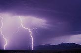 Lightning bolts brighten a rain curtain in front of a mountain 