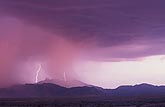 Sunset casts a pink glow on rain showers with embedded lightning