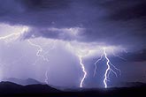 Intense, branched lightning bolts beside an illuminated rainstorm