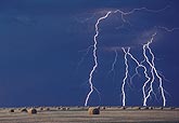 Brilliant close lightning bolts in daylight over bales of hay
