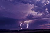 Cloud-to-ground lightning bolts in a purple sky at twilight
