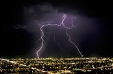 A forked cloud-to-ground lightning discharge over an urban landscape