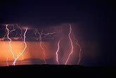 Lightning discharges trace silver filaments across a fiery sunset sky