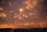 Red and gold sunset-lit Mammatus clouds with a rainbow