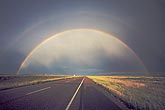 A full rainbow with secondary bow arches over a highway