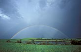 A full rainbow arcs over a peaceful farm pond