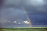 A rainbow arcs over green pastures and sunbeams paint hope in a dark and stormy sky