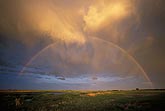 Golden twilight brushes clouds as a rainbow arcs over a farm pond