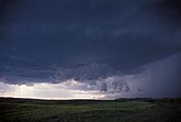 A dark cloud looms over fields under a stormy sky