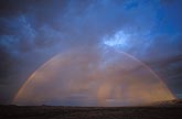 A full rainbow arcs over sunset lit rain shafts 